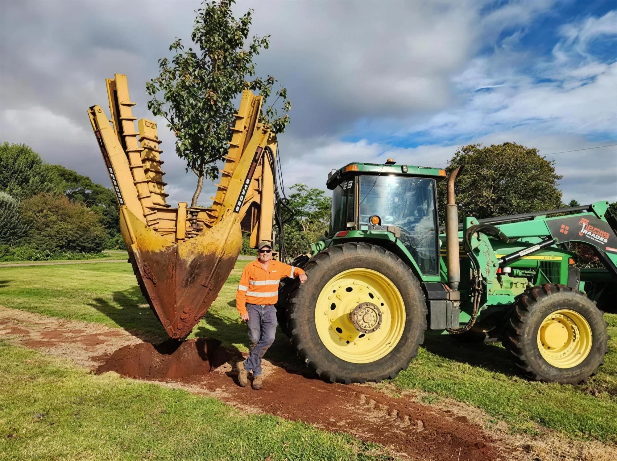 A tree spade positioned over a prepared planting hole
